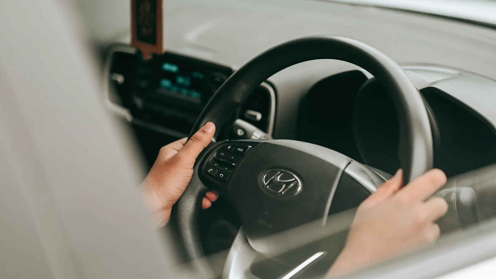 Interior de carro sedã estacionado em rua residencial. Painel frontal mostra central multimídia com tela grande de 7 a 8 polegadas exibindo mapa do GPS. Mão de motorista próxima ao volante. Luz natural do dia ilumina o console. Cena tranquila e cotidiana.