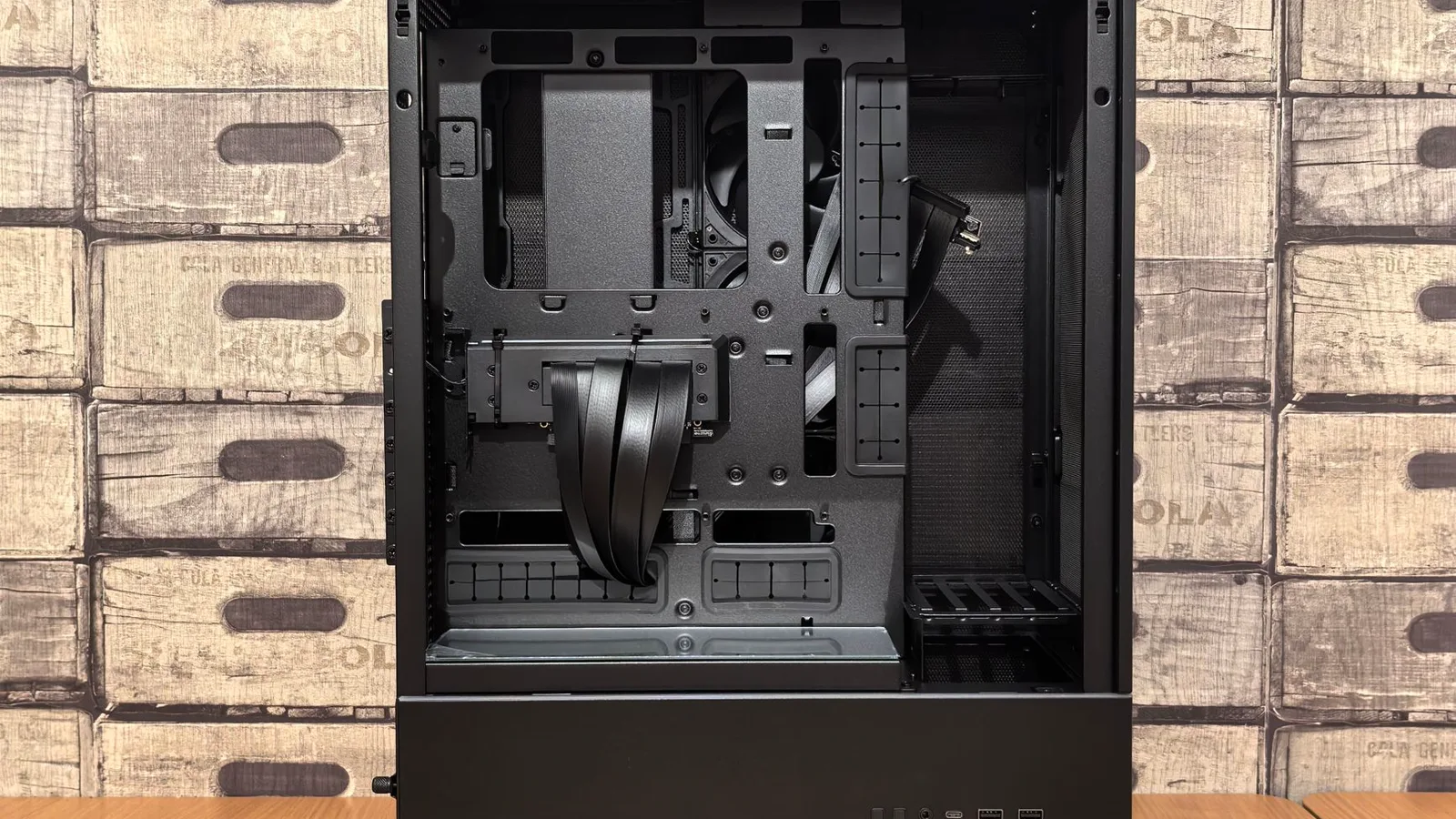 Mesa de trabalho com gabinete de computador aberto exibindo SSD M.2 NVMe, dissipador de alumínio metálico, almofada térmica, régua para medir altura e manual da placa-mãe; mão com pulseira antiestática segura chave de fenda ao lado.