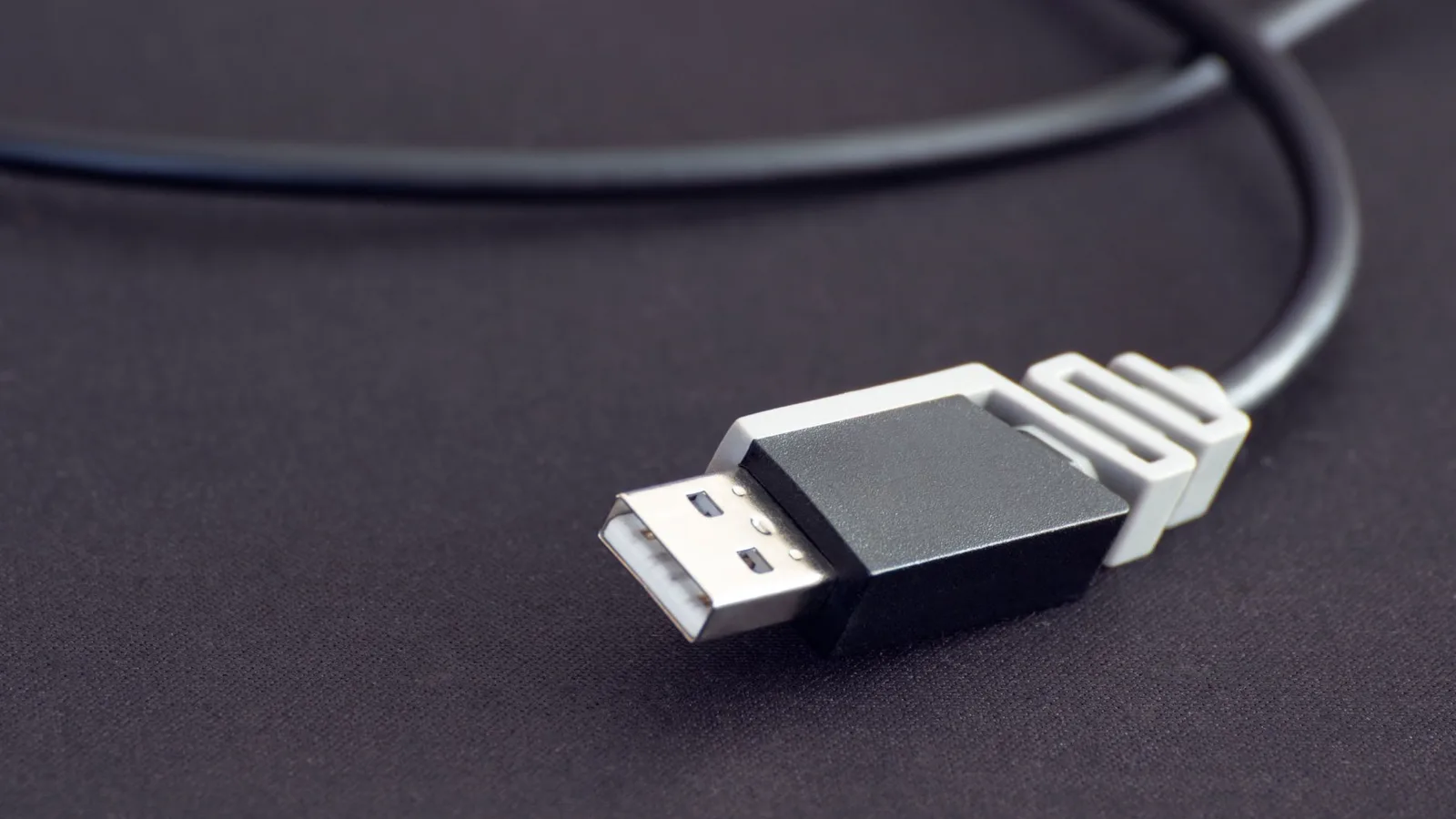 Detalhe de porta USB-A preta em computador desktop antigo, com mão de pessoa segurando pen drive prestes a conectar, papéis de nota fiscal sobre mesa de madeira ao fundo, iluminação de balcão de loja