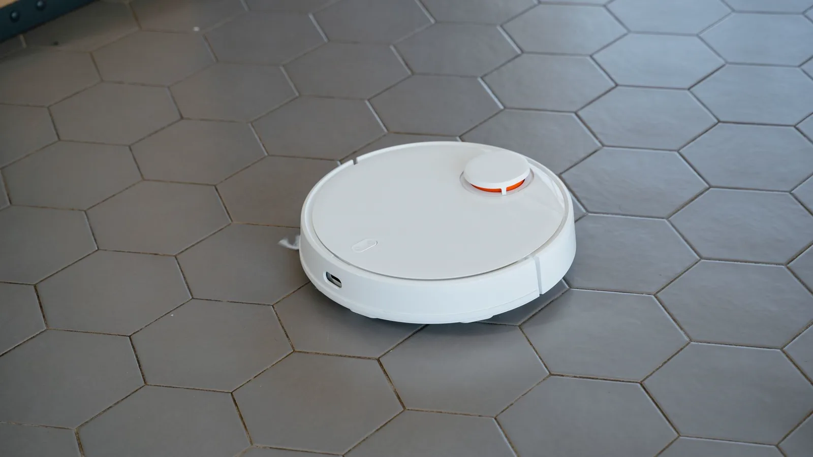 Robô aspirador preto em movimento sobre piso de cerâmica em sala de estar com luz natural
