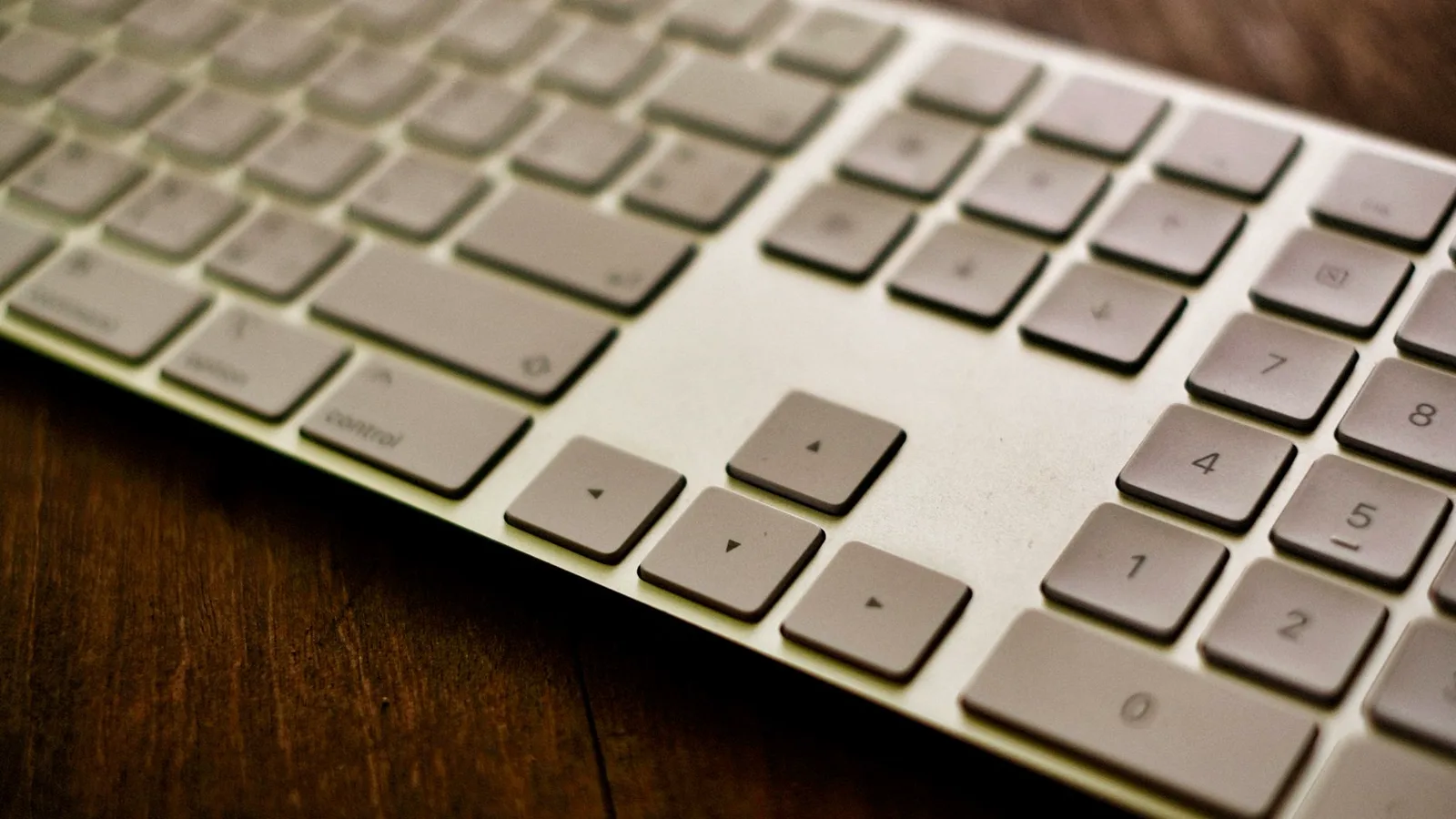 Vista de uma mesa com teclado e mouse sem fio, uma mão digitando no teclado, cenário de escritório doméstico com luz natural